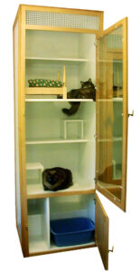 A wooden cabinet with open doors contains two cats on separate shelves, various items, and a blue litter box at the bottom.