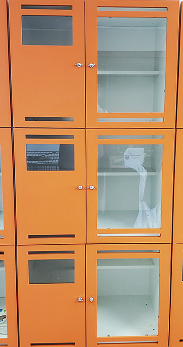 Orange lockers with glass doors, some compartments are empty, one has a wire basket and cloth inside.